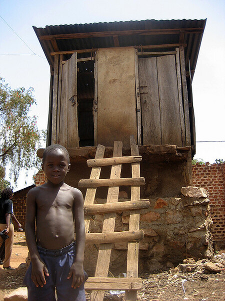 Ugandský chlapec stojí před latrínou ve slumu ve městě Kampala. Latrína je záměrně vystavěna do výšky, aby byla uchráněna před pravidelnými záplavami a nedošlo ke kontaminaci spodních vod. Nevýhodou je, že latrína je v podstatě nedostupná pro staré, handicapované, nebo pro malé děti.