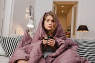 žena pod dekou pije čaj