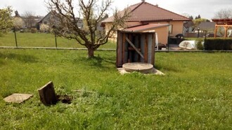 V popředí je odkryta zasakovací jímka, do které je svedena dešťová voda ze střech. V pozadí je studna, která je touto vodou dotována.