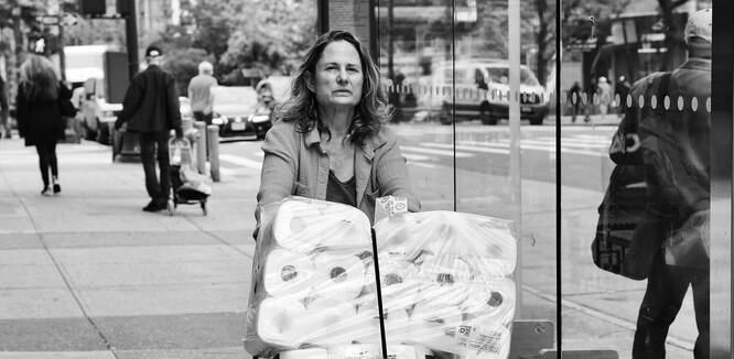 Žena veze část nákupu toaletního papíru ke svému vozu na parkovišti. Černobílý snímek pro zvýšení ponurosti.