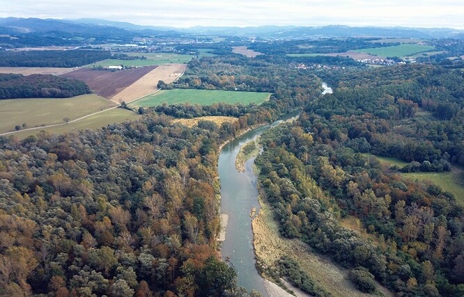 Řeka Bečva pod Choryní teče širokým korytem s mohutnými štěrkovými náplavy. V dálce je vidět Valašské Meziříčí a areál firmy DEZA.