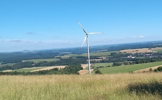Decentralizované větrné turbíny a farmy by i u nás mohly přispět k přechodu k nízkoemisní elektroenergetice. V popředí osamělá turbína v Jizerských horách, v pozadí nalevo od ní pak skupina turbín v Polsku.