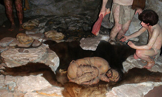 Nejstarší dosud známý doklad vazeb mezi člověkem a medvědem pochází z doby vzdálené více jak 80 tisíc let a jedná se o společný hrob neandrtálce a medvěda. Na snímku rekonstrukce pohřbu neandrtálce ve francouzské jeskyni Regourdou, uloženého na medvědí kůži. V hrobě byly nalezeny umělecky opracované medvědí kosti